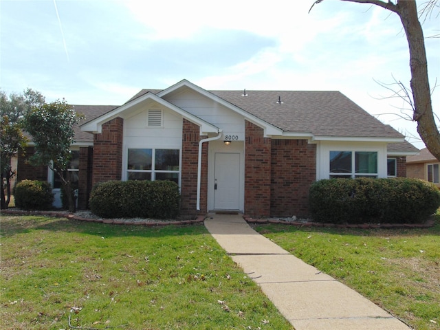 view of front facade with brick siding, a front lawn, and roof with shingles