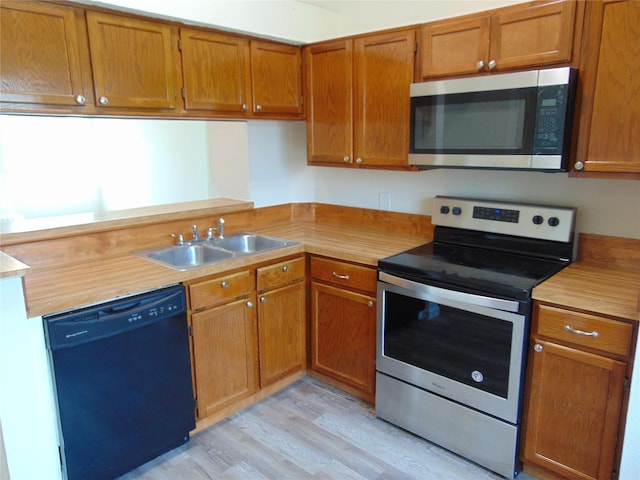 kitchen featuring appliances with stainless steel finishes, light wood-type flooring, a sink, and brown cabinets