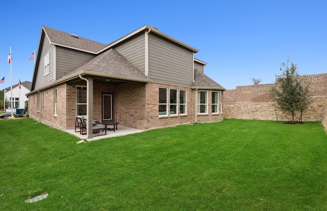 rear view of property featuring a shingled roof, a patio area, brick siding, and a lawn