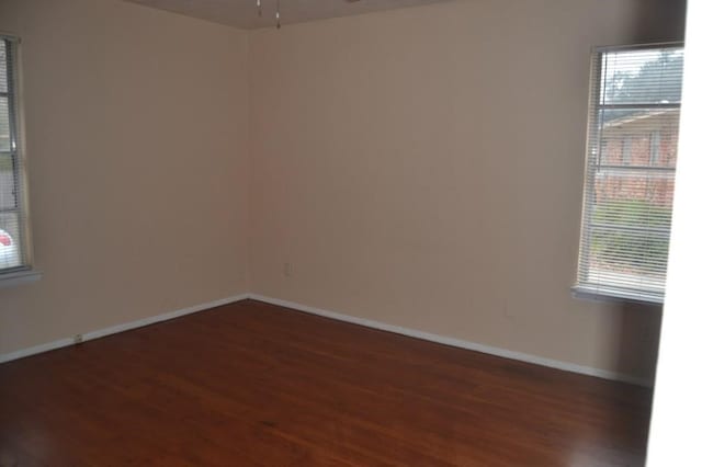 empty room featuring dark wood finished floors, baseboards, and ceiling fan