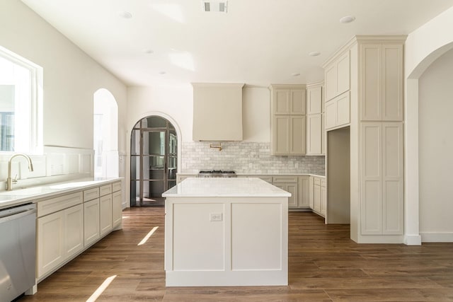 kitchen featuring arched walkways, wood finished floors, a sink, stainless steel dishwasher, and backsplash