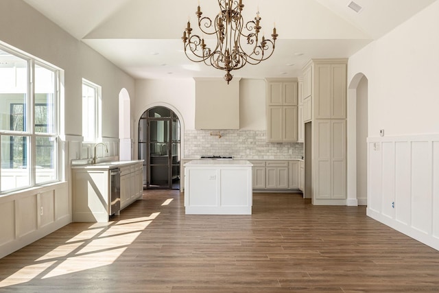 kitchen with arched walkways, visible vents, vaulted ceiling, a center island, and tasteful backsplash