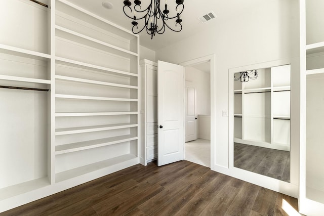 spacious closet with dark wood-type flooring, visible vents, and an inviting chandelier