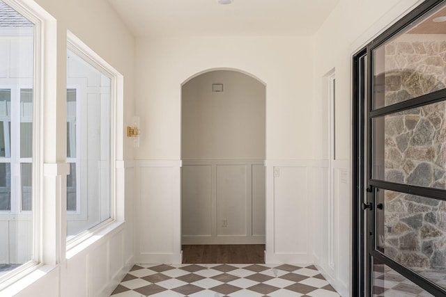 hallway with light floors, arched walkways, a decorative wall, and a wainscoted wall