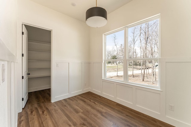 unfurnished dining area featuring dark wood-style floors, a wealth of natural light, and a decorative wall