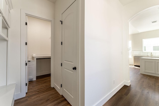 hallway with arched walkways, dark wood-style flooring, visible vents, and baseboards