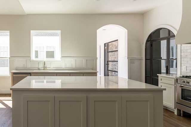 kitchen featuring wall oven, a wainscoted wall, dark wood-type flooring, stainless steel dishwasher, and a sink