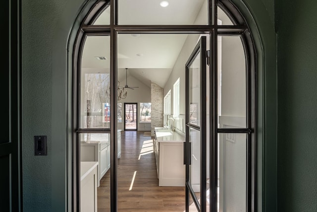 hall featuring lofted ceiling, a textured wall, wood finished floors, and a sink