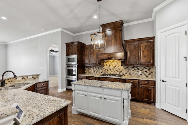 kitchen with a center island, arched walkways, custom range hood, appliances with stainless steel finishes, and a sink