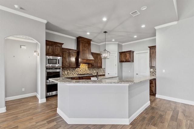 kitchen with arched walkways, stainless steel appliances, a spacious island, custom range hood, and visible vents