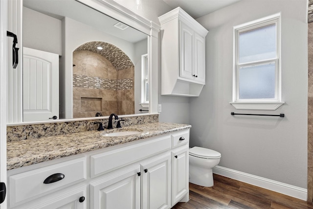 bathroom featuring baseboards, toilet, wood finished floors, a tile shower, and vanity