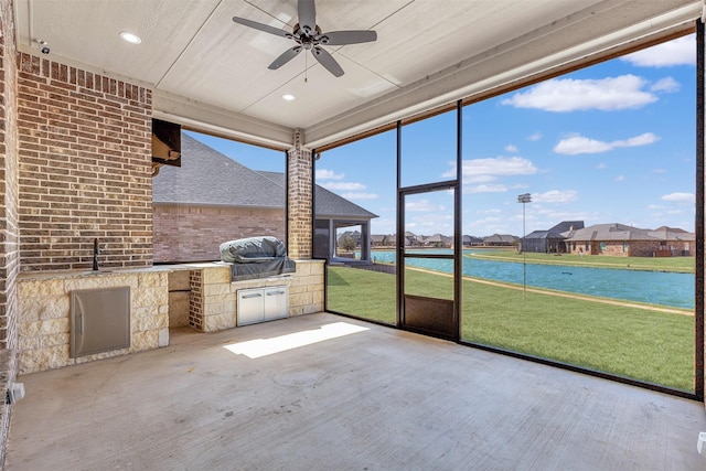 unfurnished sunroom featuring ceiling fan, a water view, and a sink