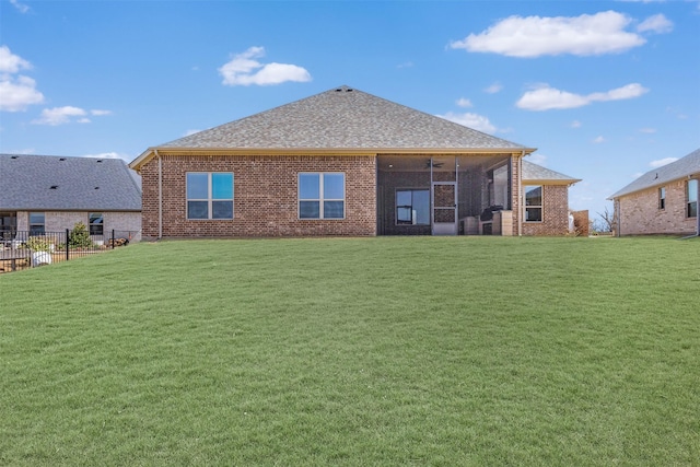 rear view of house featuring a sunroom, roof with shingles, a lawn, and brick siding