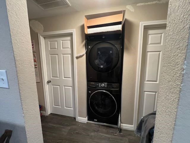 clothes washing area with laundry area, dark wood-type flooring, visible vents, baseboards, and stacked washer / drying machine