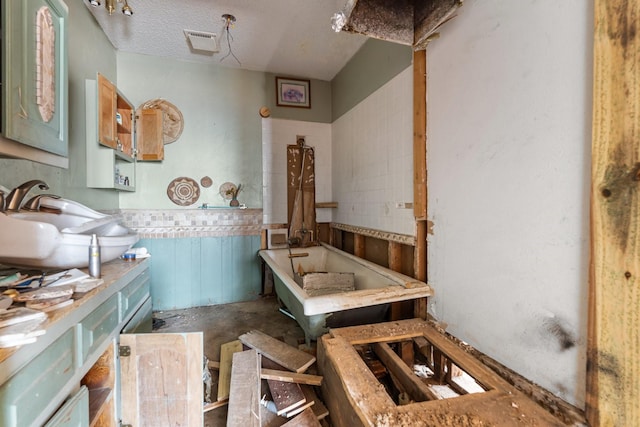 bathroom featuring a textured ceiling, a washtub, a sink, visible vents, and wainscoting