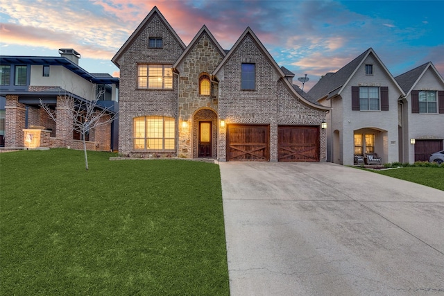 french country style house with brick siding, a yard, a garage, stone siding, and driveway