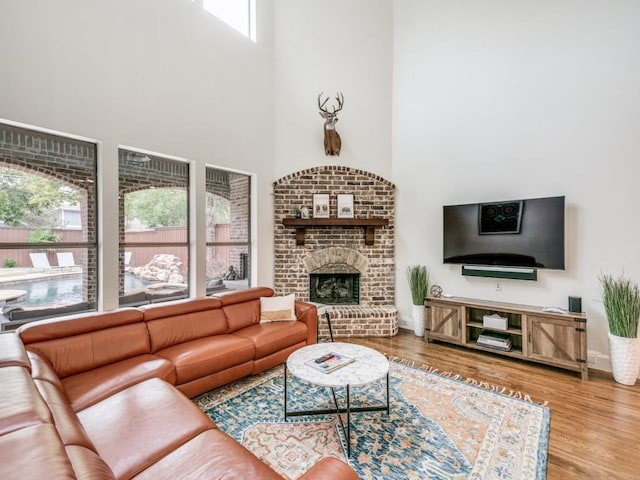 living room with a high ceiling, a brick fireplace, wood finished floors, and baseboards