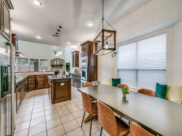 kitchen featuring light tile patterned floors, stainless steel microwave, ornamental molding, a kitchen island, and dark brown cabinetry