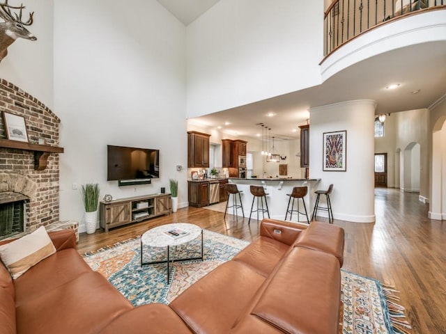 living room with arched walkways, a fireplace, a high ceiling, wood finished floors, and baseboards