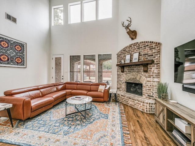 living room featuring visible vents, a fireplace, a towering ceiling, and wood finished floors