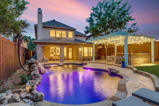 back of property at dusk featuring a chimney, brick siding, outdoor dry bar, and a fenced backyard