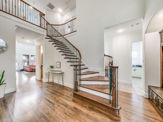 staircase featuring visible vents, a towering ceiling, baseboards, and wood finished floors