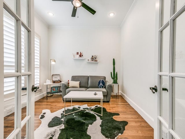 living area with french doors, crown molding, light wood-style flooring, ceiling fan, and baseboards