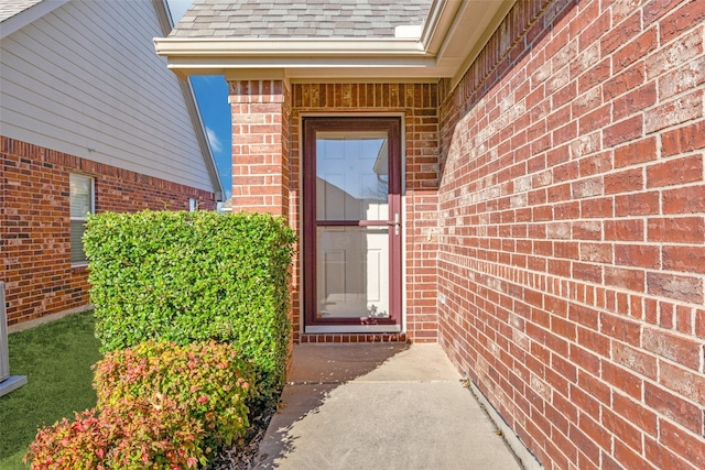 doorway to property featuring roof with shingles and brick siding