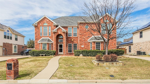 traditional-style house with roof with shingles, a front yard, central AC unit, and brick siding