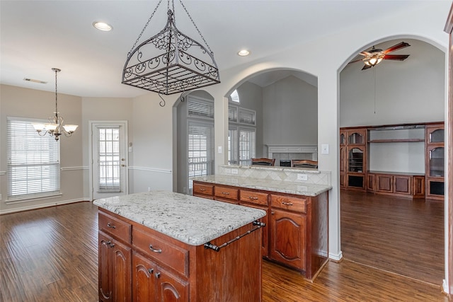 kitchen with recessed lighting, ceiling fan with notable chandelier, a kitchen island, dark wood-style floors, and brown cabinetry