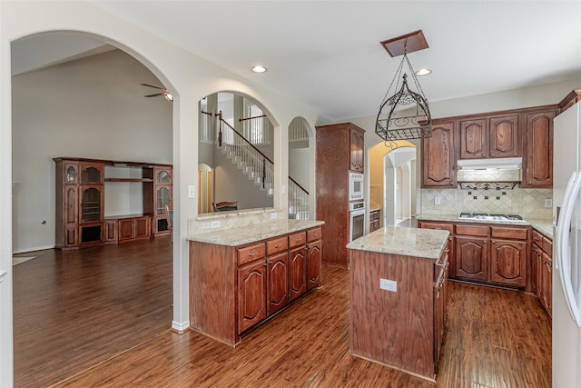 kitchen featuring dark wood-style floors, arched walkways, a center island, white appliances, and under cabinet range hood