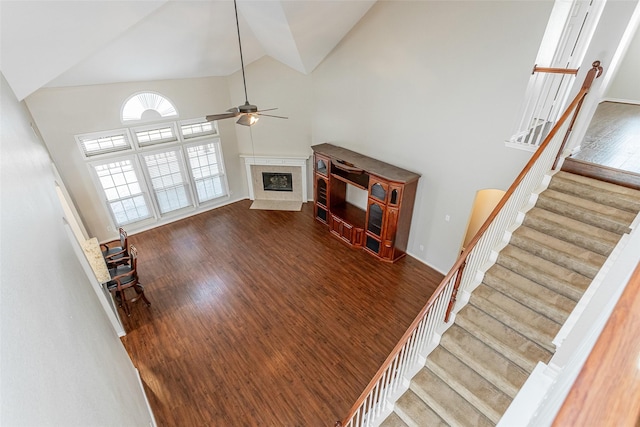 unfurnished living room with ceiling fan, high vaulted ceiling, a fireplace, wood finished floors, and stairway