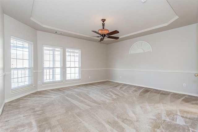 carpeted spare room featuring baseboards, visible vents, a tray ceiling, and a ceiling fan