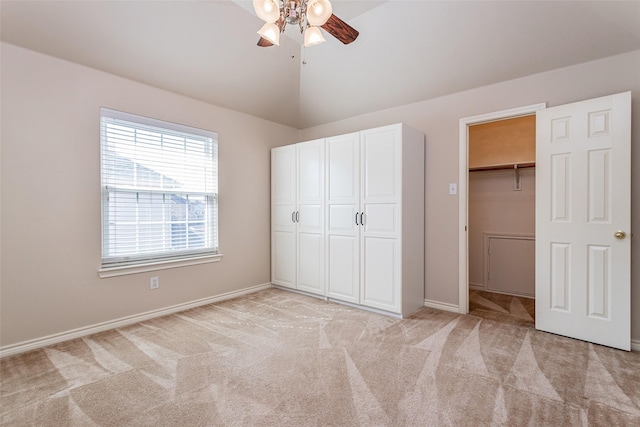 unfurnished bedroom featuring light carpet, a ceiling fan, vaulted ceiling, a spacious closet, and a closet