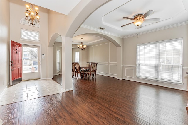 entrance foyer with visible vents, wood finished floors, crown molding, a decorative wall, and ceiling fan with notable chandelier