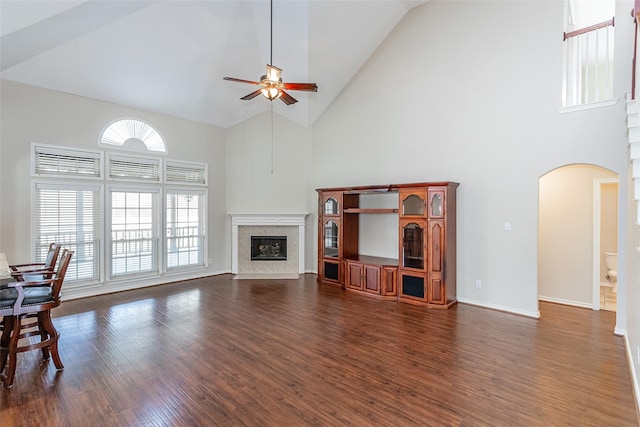 living room featuring arched walkways, dark wood-style flooring, a premium fireplace, a ceiling fan, and high vaulted ceiling