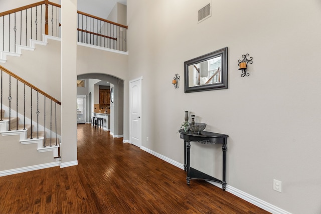 entryway featuring arched walkways, wood finished floors, visible vents, baseboards, and stairs