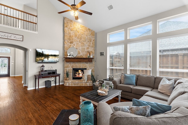 living room with arched walkways, a fireplace, visible vents, wood finished floors, and baseboards