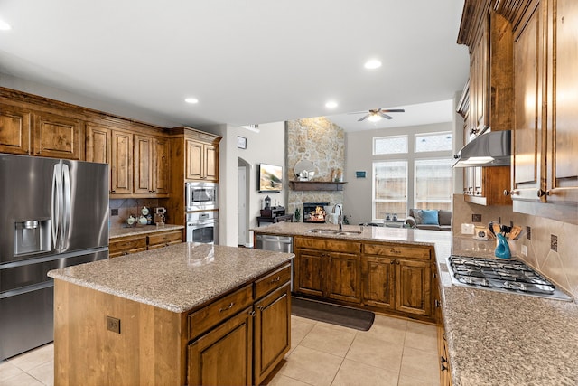 kitchen with light tile patterned floors, under cabinet range hood, stainless steel appliances, a sink, and open floor plan