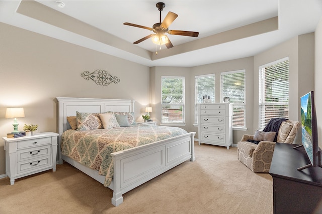 bedroom featuring baseboards, a tray ceiling, ceiling fan, and light colored carpet