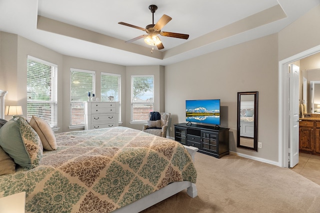 bedroom with light carpet, ensuite bath, multiple windows, and a raised ceiling