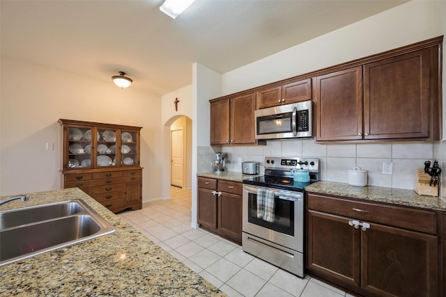 2278 Bryant Ln, Fate, TX 75189 - kitchen with stainless steel appliances, a sink, arched walkways, light tile patterned floors, and backsplash