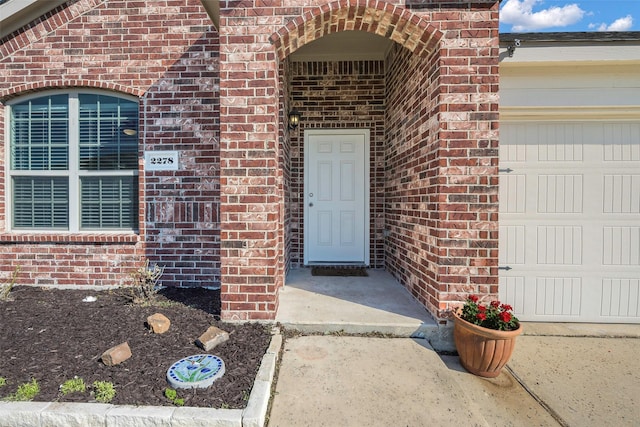 entrance to property featuring a garage and brick siding