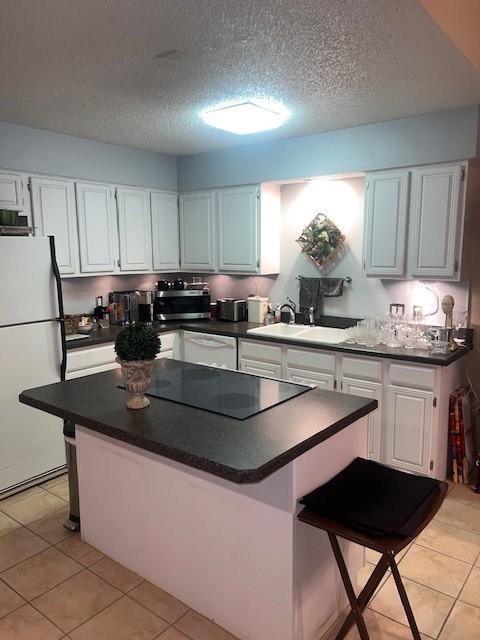 kitchen with white appliances, a sink, white cabinets, a center island, and dark countertops