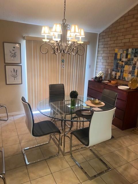 dining room featuring light tile patterned flooring, vaulted ceiling, brick wall, a chandelier, and baseboards