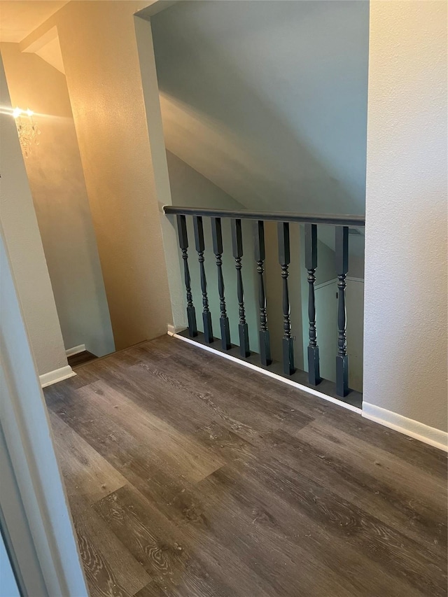 staircase featuring lofted ceiling, a textured wall, and wood finished floors