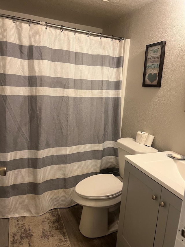 bathroom with toilet, vanity, wood finished floors, and a textured wall