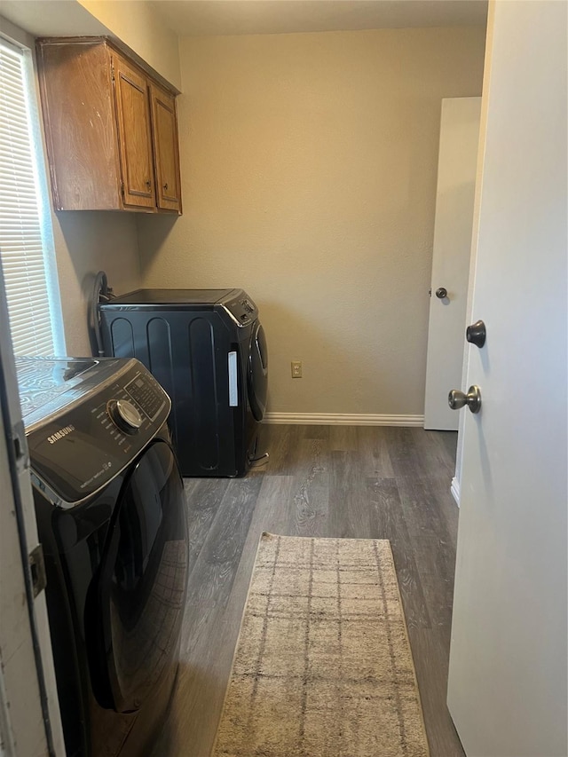 laundry area featuring dark wood-type flooring, washing machine and dryer, cabinet space, and baseboards