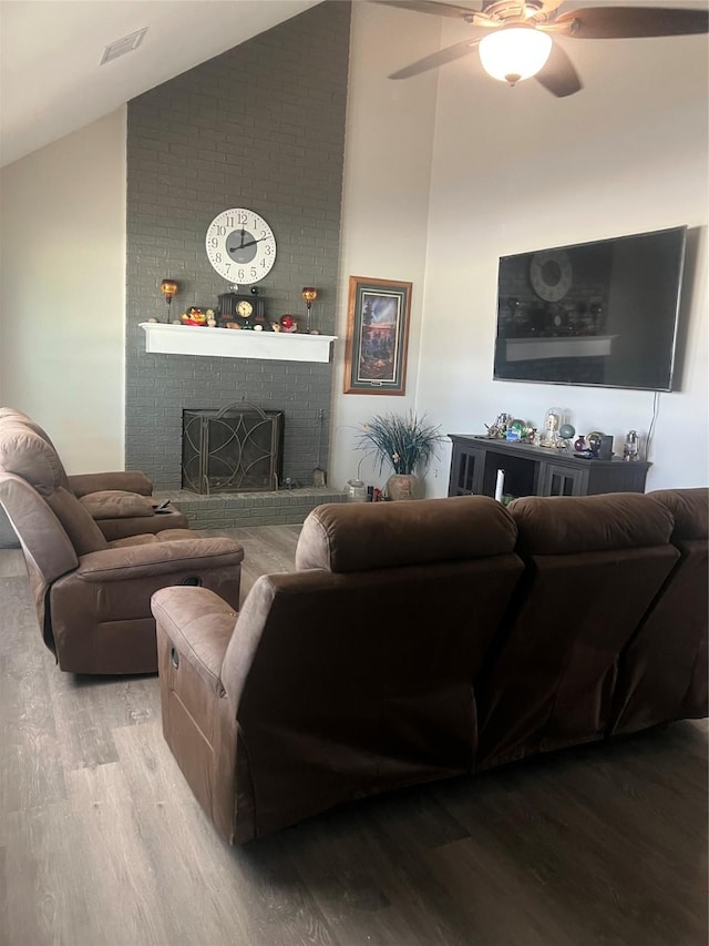 living area with visible vents, a ceiling fan, wood finished floors, a brick fireplace, and high vaulted ceiling