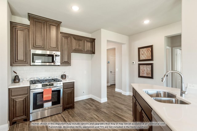 kitchen featuring decorative backsplash, dark wood-style flooring, stainless steel appliances, light countertops, and a sink